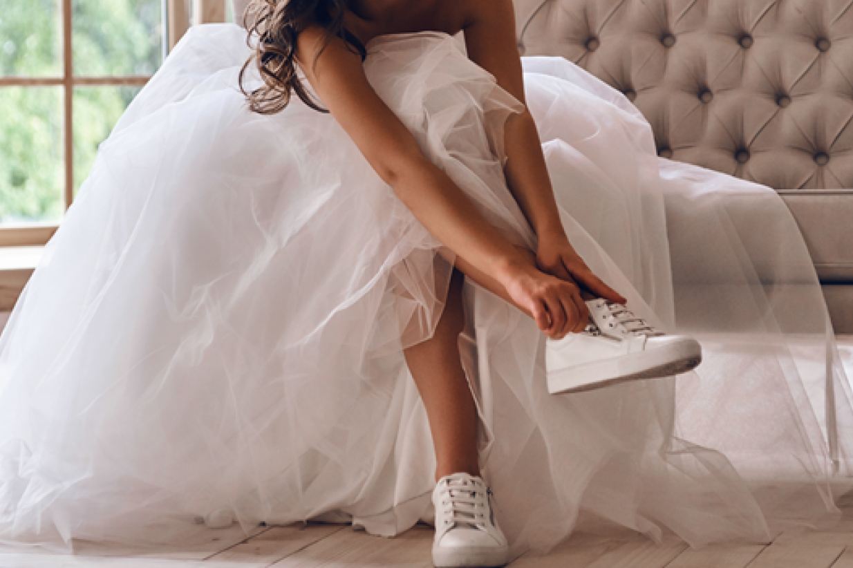 a modern bride  wearing a wedding dress puts on sneakers