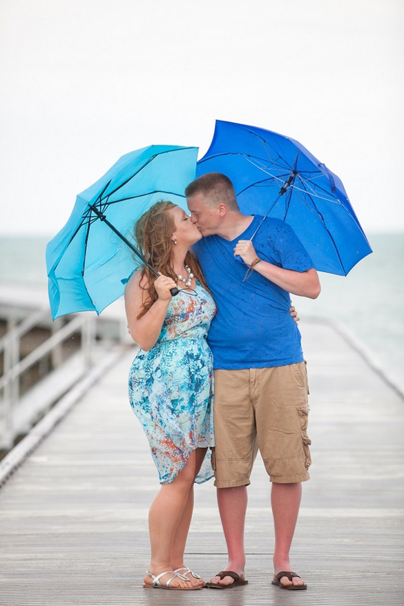 Rainy beach engagement photos with blue umbrellas