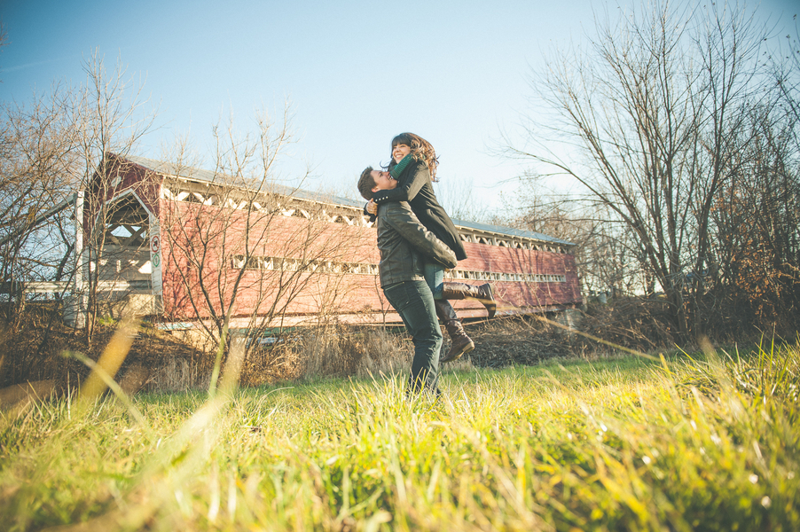Rustic engagement photo of couple by an old covered bridge